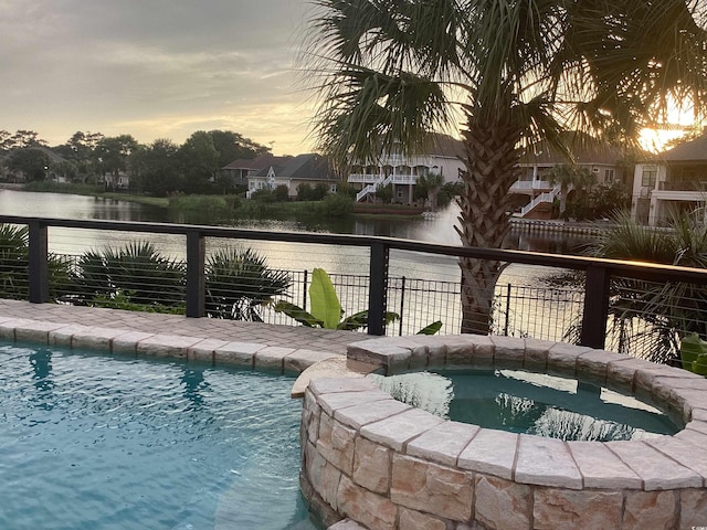 pool at dusk with a water view and an in ground hot tub