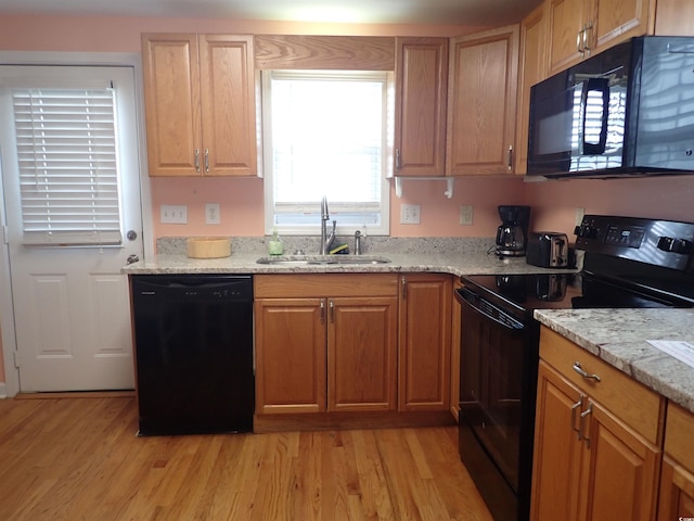 kitchen with light stone countertops, light wood-type flooring, black appliances, and sink