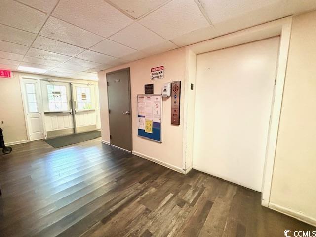 interior space with a paneled ceiling and dark hardwood / wood-style floors