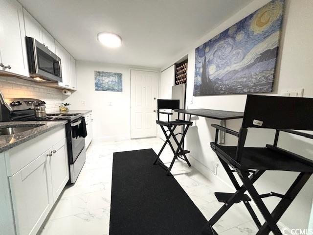 kitchen featuring stainless steel appliances, dark stone countertops, white cabinets, and backsplash