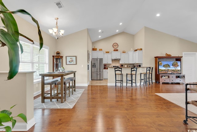 dining area with light wood-type flooring, high vaulted ceiling, and a notable chandelier