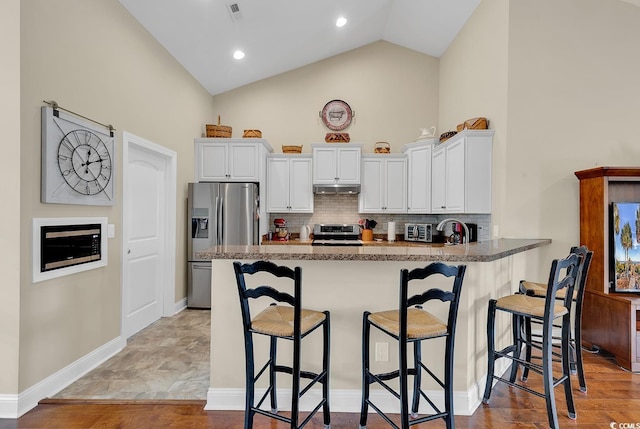 kitchen featuring appliances with stainless steel finishes, a peninsula, a kitchen bar, white cabinetry, and stone countertops
