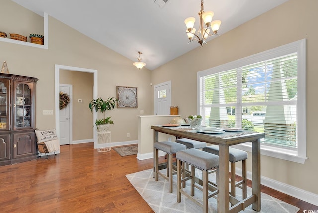 dining area with baseboards, wood finished floors, a notable chandelier, and vaulted ceiling