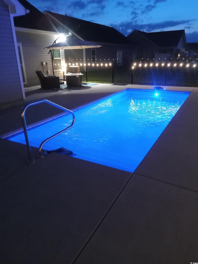 pool at night with a patio area, outdoor lounge area, fence, and a fenced in pool
