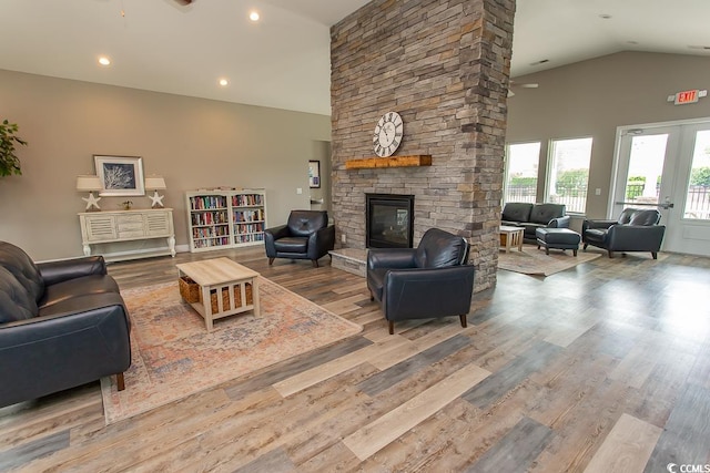 living room with ceiling fan, french doors, a stone fireplace, high vaulted ceiling, and light hardwood / wood-style floors