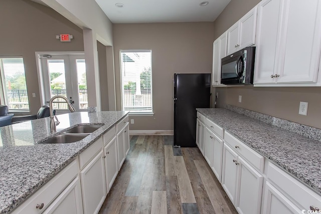 kitchen featuring light hardwood / wood-style floors, white cabinetry, light stone counters, black appliances, and sink