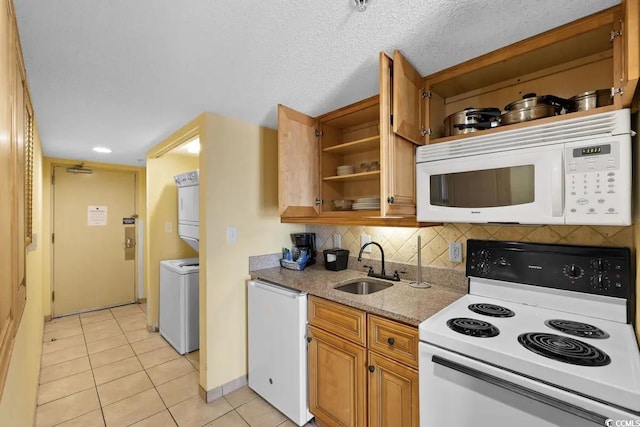 kitchen featuring stacked washing maching and dryer, light tile patterned floors, sink, a textured ceiling, and white appliances