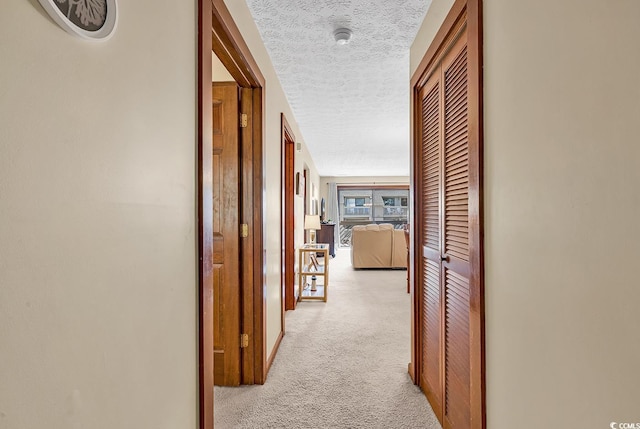 hall with light colored carpet and a textured ceiling