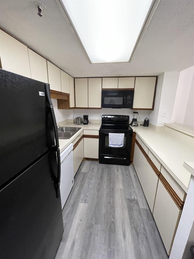 kitchen featuring light wood-type flooring, cream cabinets, sink, a textured ceiling, and black appliances