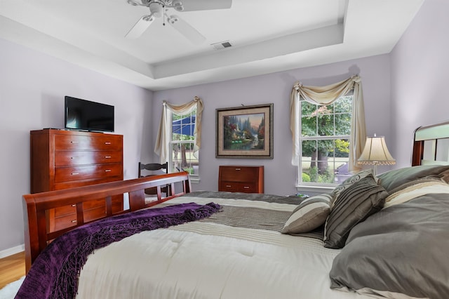 bedroom with multiple windows, light wood-type flooring, a raised ceiling, and ceiling fan