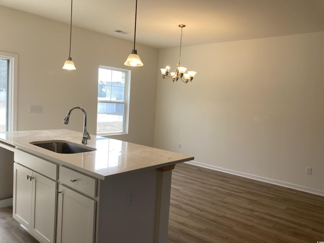 kitchen featuring a kitchen island with sink, a sink, baseboards, hanging light fixtures, and dark wood-style floors