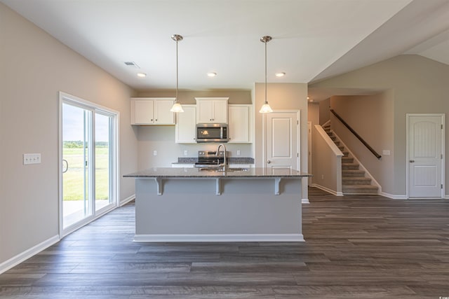 kitchen featuring a kitchen island with sink, hanging light fixtures, appliances with stainless steel finishes, and dark stone counters