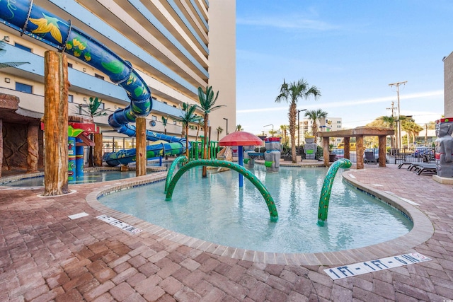 community pool with a water play area, a water slide, and a patio