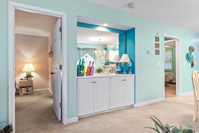 corridor with a textured ceiling, an inviting chandelier, and light colored carpet