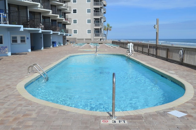 pool with a patio, fence, and a water view