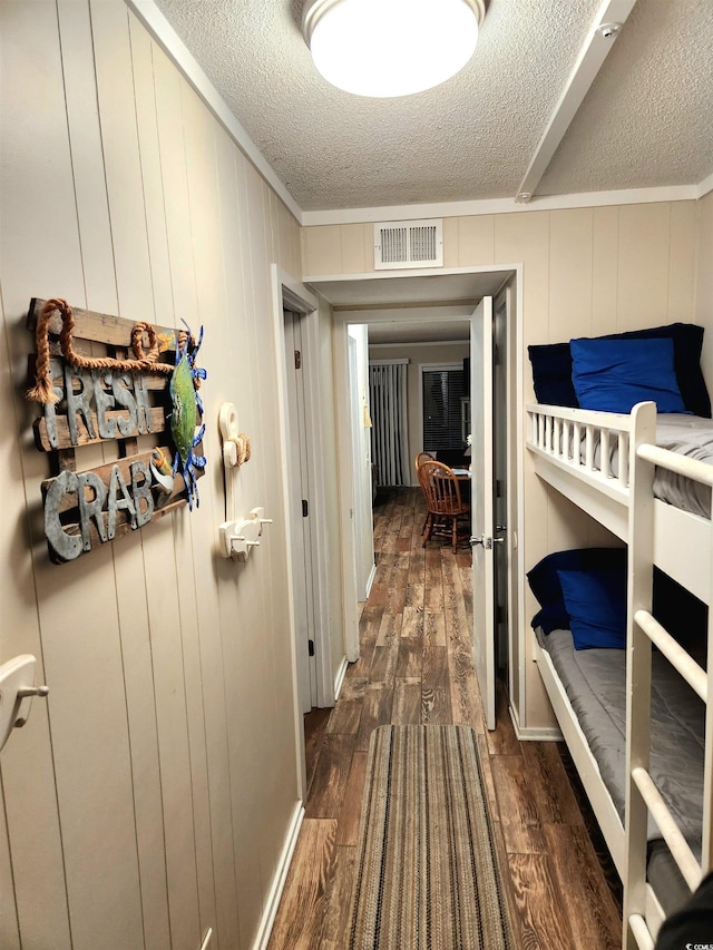 corridor with ornamental molding, dark wood-style flooring, visible vents, and a textured ceiling