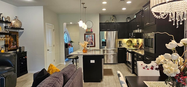 kitchen featuring light wood-type flooring, pendant lighting, a notable chandelier, a center island with sink, and stainless steel appliances