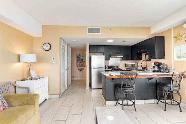 kitchen with a breakfast bar area, kitchen peninsula, appliances with stainless steel finishes, and light tile patterned floors