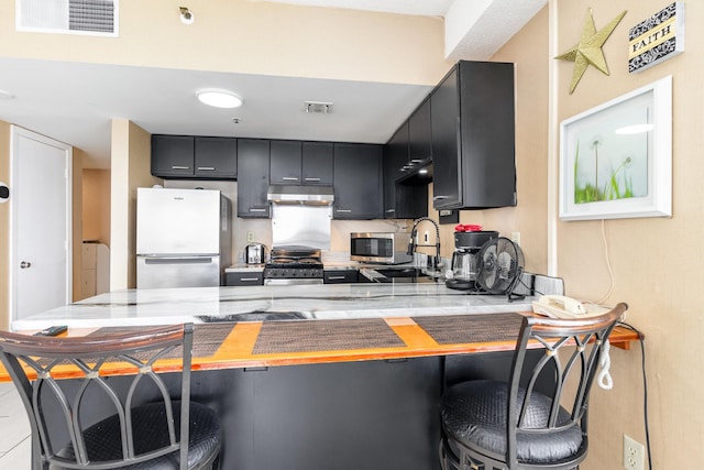 kitchen with light stone countertops, stove, kitchen peninsula, a breakfast bar, and white refrigerator