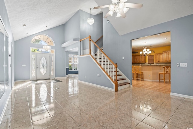 foyer entrance featuring light tile patterned flooring, a textured ceiling, high vaulted ceiling, and ceiling fan with notable chandelier