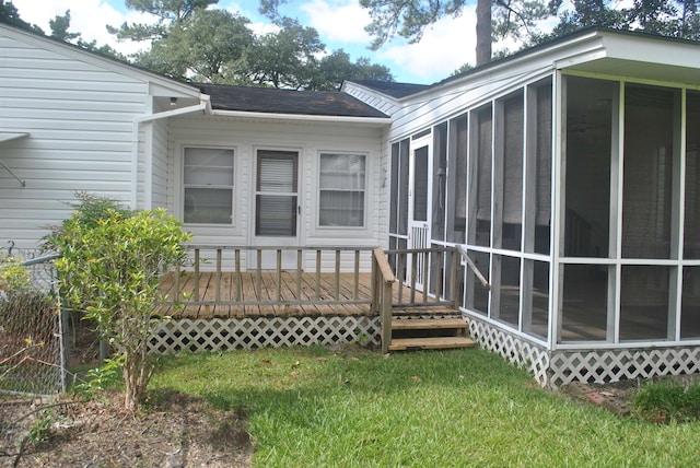 rear view of property featuring a lawn, a deck, and a sunroom