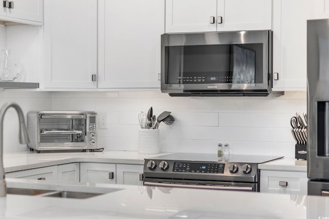 kitchen with appliances with stainless steel finishes, light stone counters, white cabinetry, and backsplash