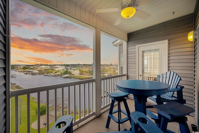 balcony at dusk with ceiling fan and a water view