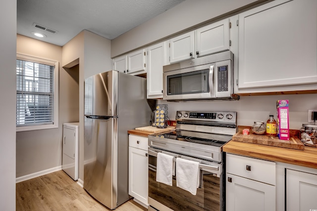 kitchen featuring wood counters, light hardwood / wood-style floors, washer / dryer, stainless steel appliances, and white cabinetry