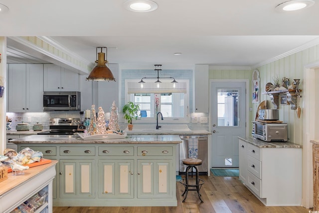 kitchen featuring sink, light hardwood / wood-style floors, stainless steel appliances, pendant lighting, and ornamental molding