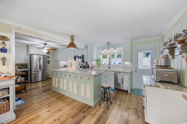 kitchen with appliances with stainless steel finishes, ornamental molding, light hardwood / wood-style floors, and pendant lighting