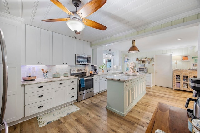 kitchen featuring light stone countertops, light wood-type flooring, a kitchen island, white cabinetry, and stainless steel appliances