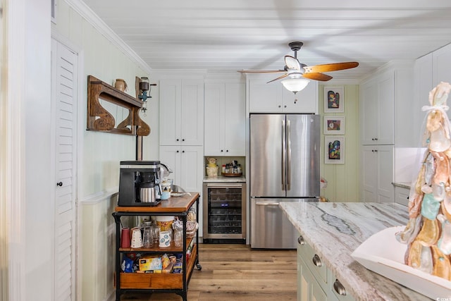 kitchen featuring beverage cooler, crown molding, stainless steel fridge, white cabinets, and light stone counters