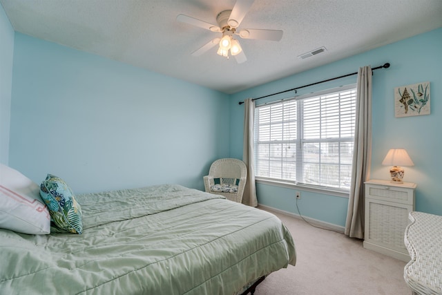 bedroom with ceiling fan, a textured ceiling, light carpet, visible vents, and baseboards