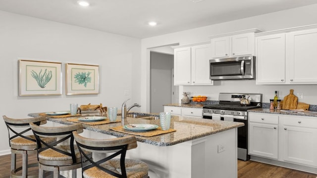 kitchen featuring a breakfast bar area, white cabinets, an island with sink, and appliances with stainless steel finishes