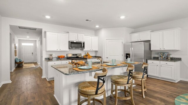 kitchen with stainless steel appliances, white cabinetry, a center island with sink, and dark wood-type flooring