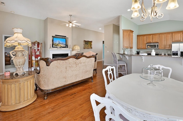 dining space with sink, wood-type flooring, ceiling fan with notable chandelier, and vaulted ceiling