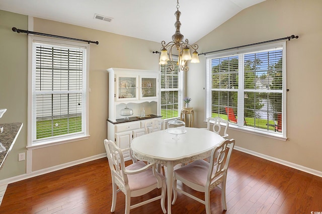 dining area featuring a chandelier, vaulted ceiling, a healthy amount of sunlight, and dark hardwood / wood-style flooring