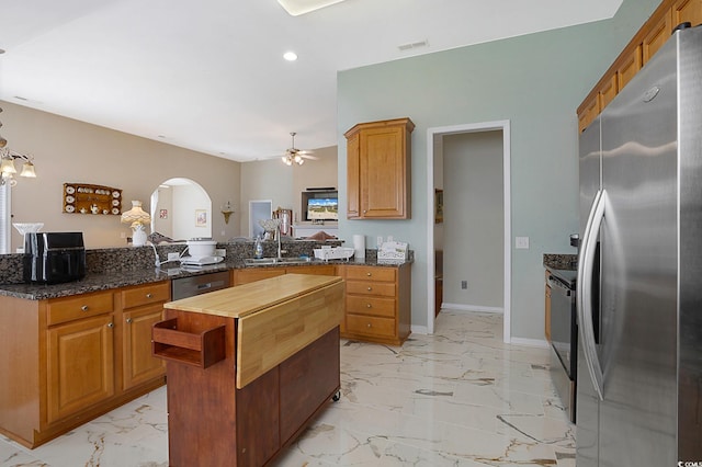 kitchen with kitchen peninsula, ceiling fan, appliances with stainless steel finishes, dark stone countertops, and sink