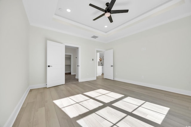 unfurnished bedroom with a tray ceiling, ceiling fan, light hardwood / wood-style flooring, and ornamental molding