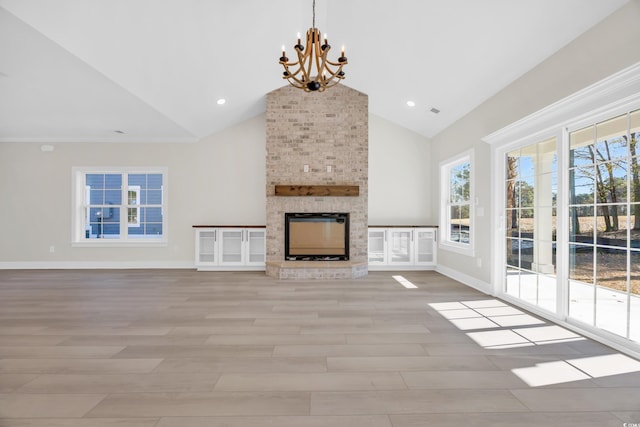 unfurnished living room with a fireplace, high vaulted ceiling, light hardwood / wood-style flooring, and a notable chandelier