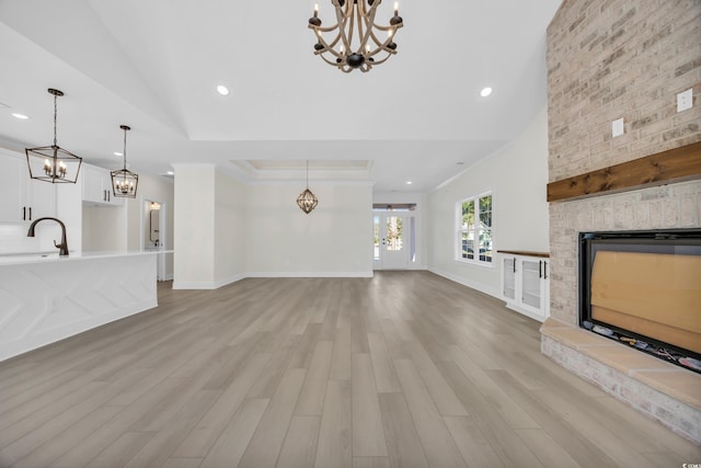 unfurnished living room featuring sink, a stone fireplace, light hardwood / wood-style floors, lofted ceiling, and ornamental molding