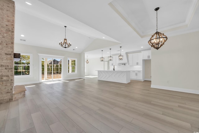 unfurnished living room with a raised ceiling, light hardwood / wood-style flooring, and an inviting chandelier