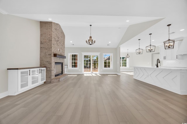 unfurnished living room featuring light hardwood / wood-style floors, a stone fireplace, sink, and high vaulted ceiling