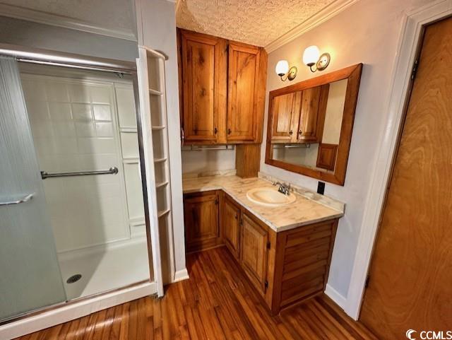 bathroom with a shower with door, vanity, a textured ceiling, crown molding, and hardwood / wood-style flooring