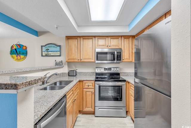 kitchen with kitchen peninsula, sink, a tray ceiling, light stone countertops, and appliances with stainless steel finishes