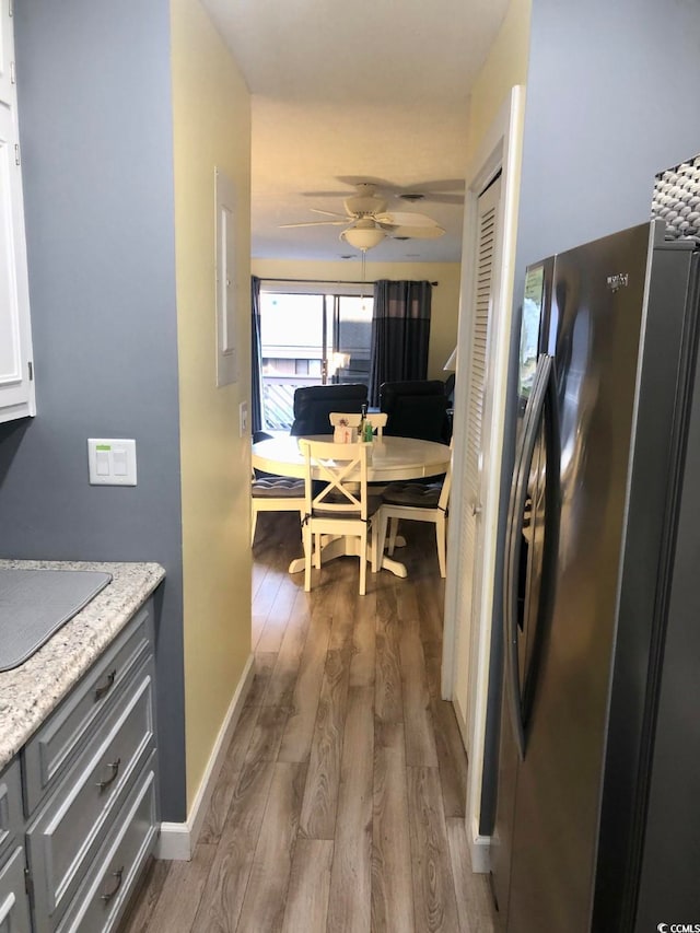 kitchen with wood-type flooring, white cabinetry, light stone countertops, ceiling fan, and stainless steel fridge