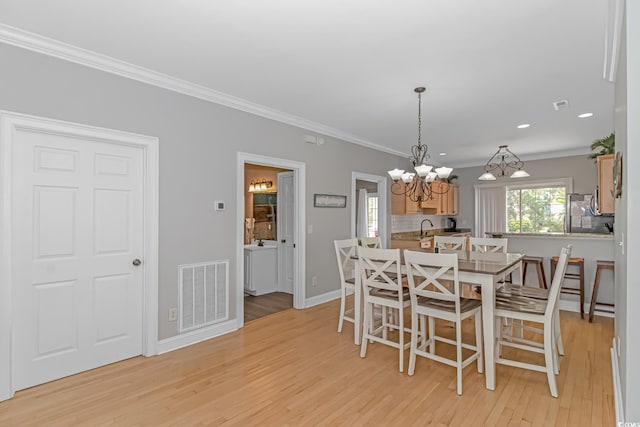 dining room with crown molding, a notable chandelier, sink, and light hardwood / wood-style floors