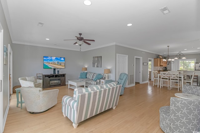 living room with ceiling fan with notable chandelier, ornamental molding, and light hardwood / wood-style floors