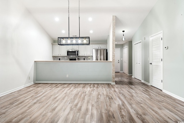 kitchen with stainless steel appliances, hanging light fixtures, light wood-type flooring, and tasteful backsplash