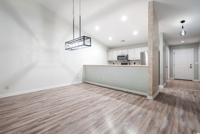 kitchen with appliances with stainless steel finishes, light wood-type flooring, pendant lighting, and white cabinets